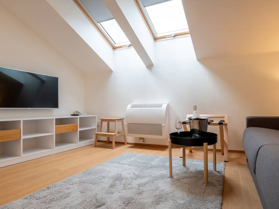 A modern loft apartment with a large TV, a built-in air conditioner, a cozy seating area, and skylights.