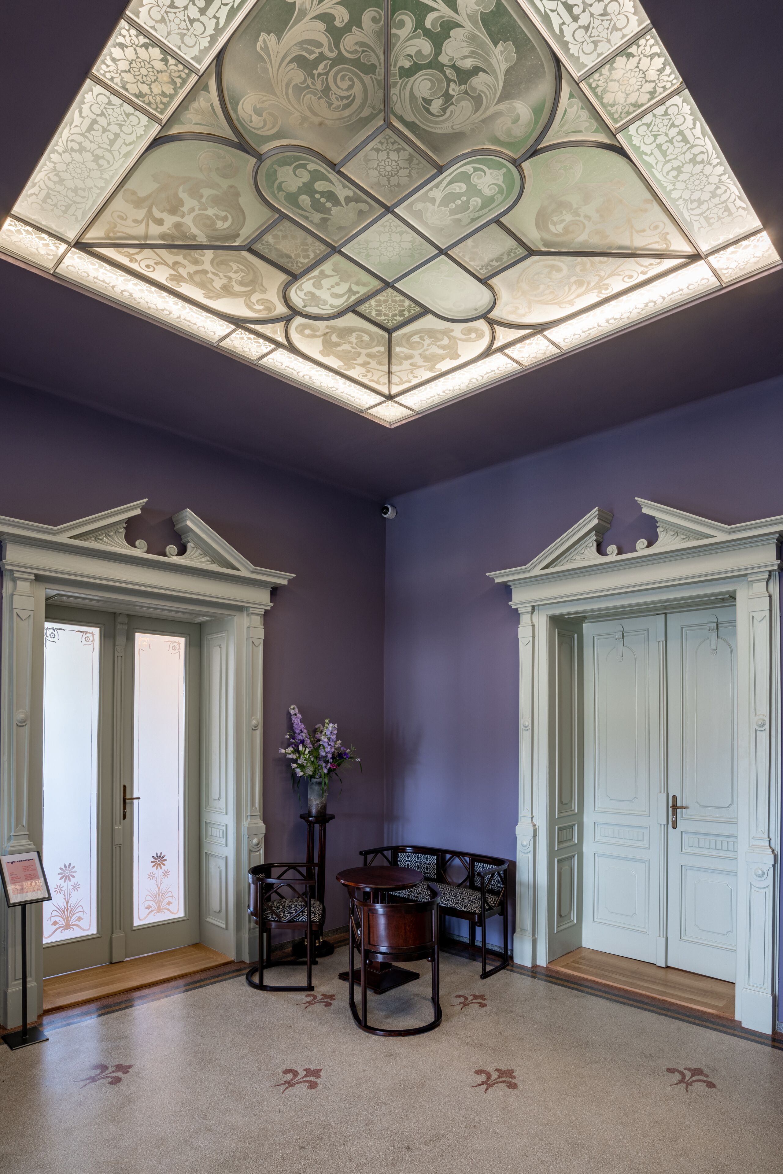 Una habitación con un techo decorativo, dos puertas blancas, un banco y una pequeña mesa con un florero.