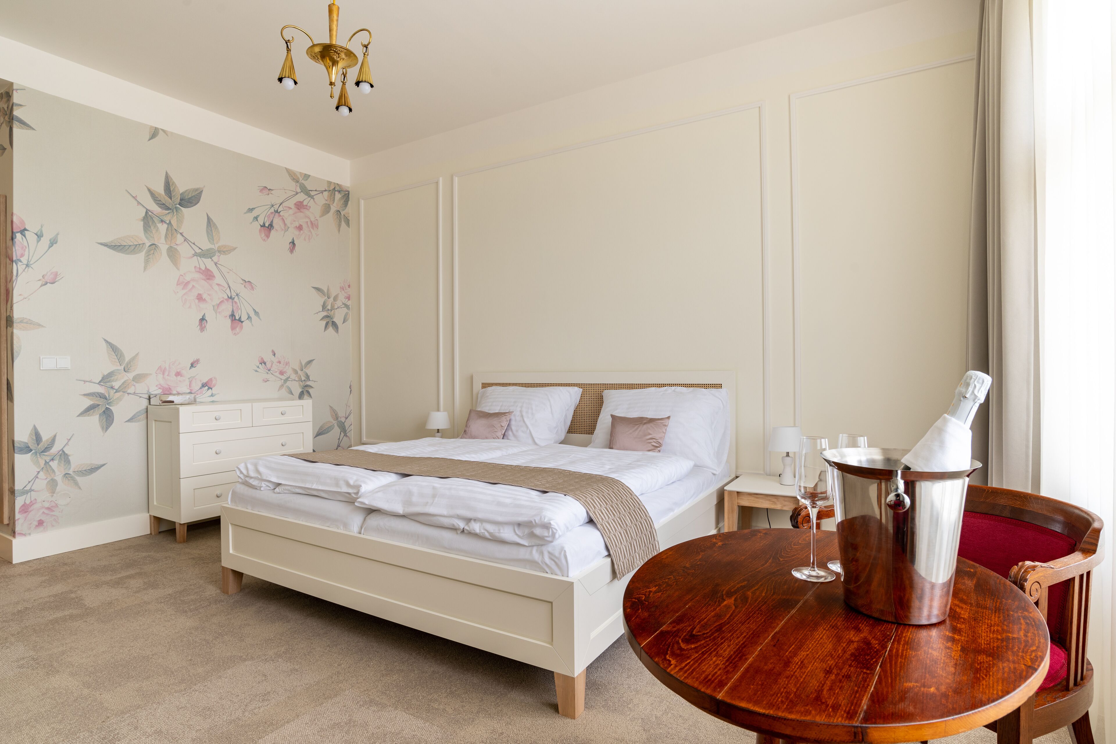 Une chambre à coucher bien rangée, avec un lit, une table de chevet et une table en bois sur laquelle se trouve une bouteille.