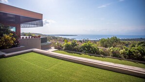 Une maison moderne avec une grande pelouse et vue sur l’océan.