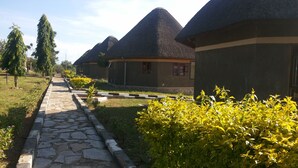 A pathway leading to a row of conical-roofed buildings with a stone pathway and greenery. - Parkside Safari Lodge (Pakwach)