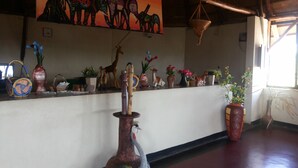 A reception area with a counter displaying various decorative items, a wall with a mural, and a hanging basket. - Parkside Safari Lodge (Pakwach)