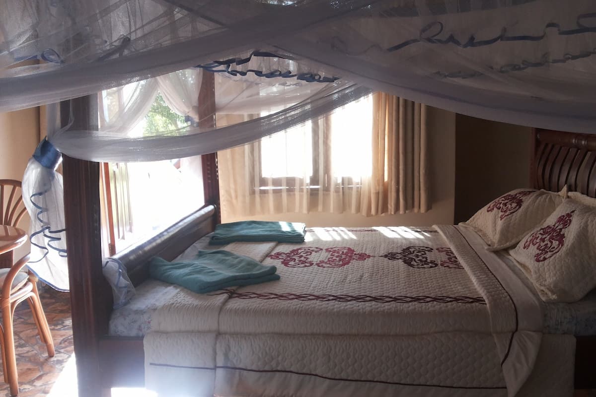 A bed with a canopy, a window with curtains, and a chair.