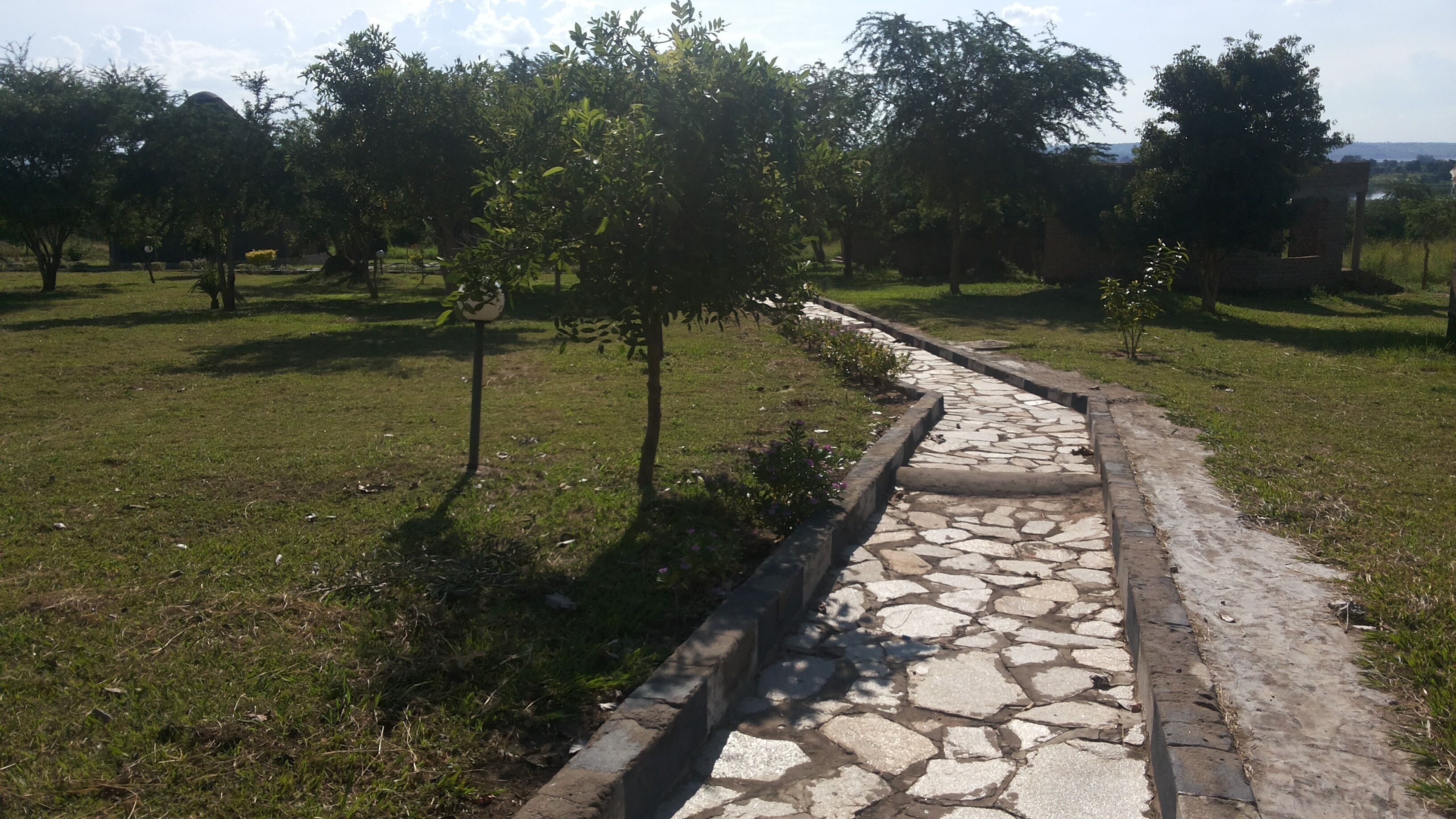 Un sendero de piedra en un área con césped, árboles y una estructura de ladrillo al fondo.