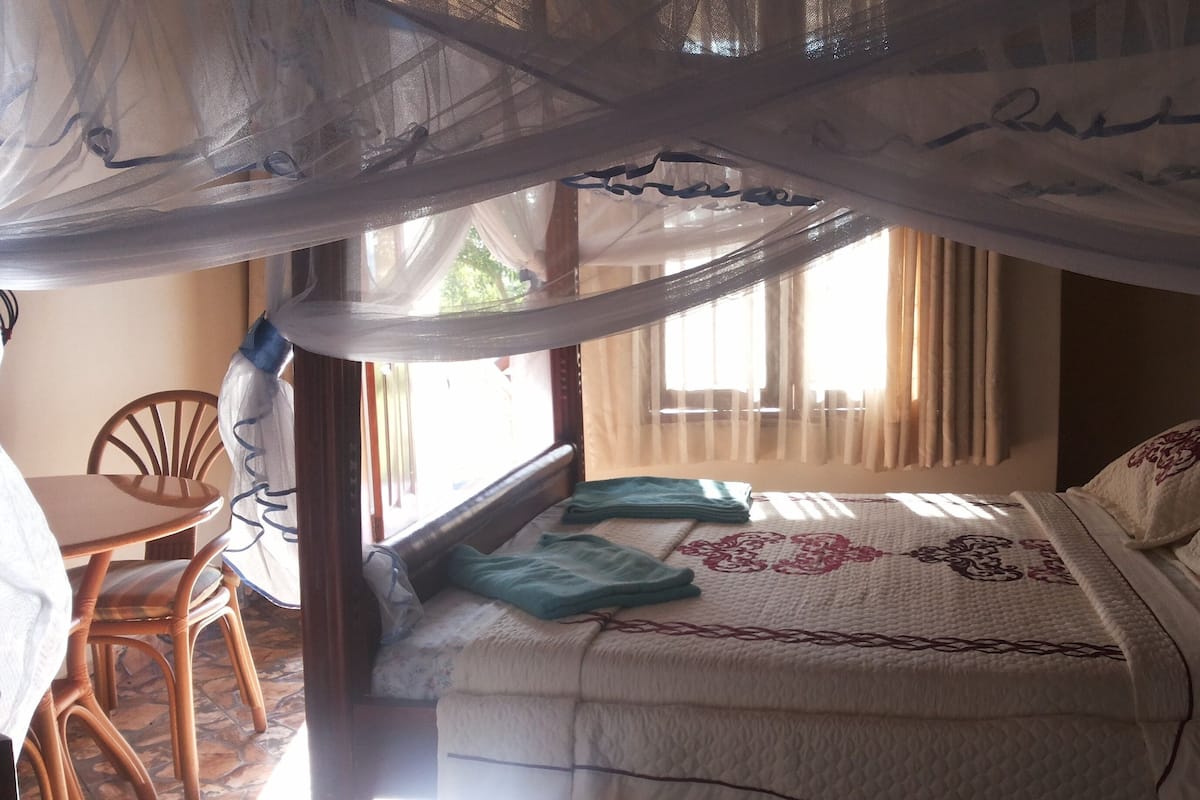 A bedroom with a bed, a chair, a window with curtains, and a mosquito net.
