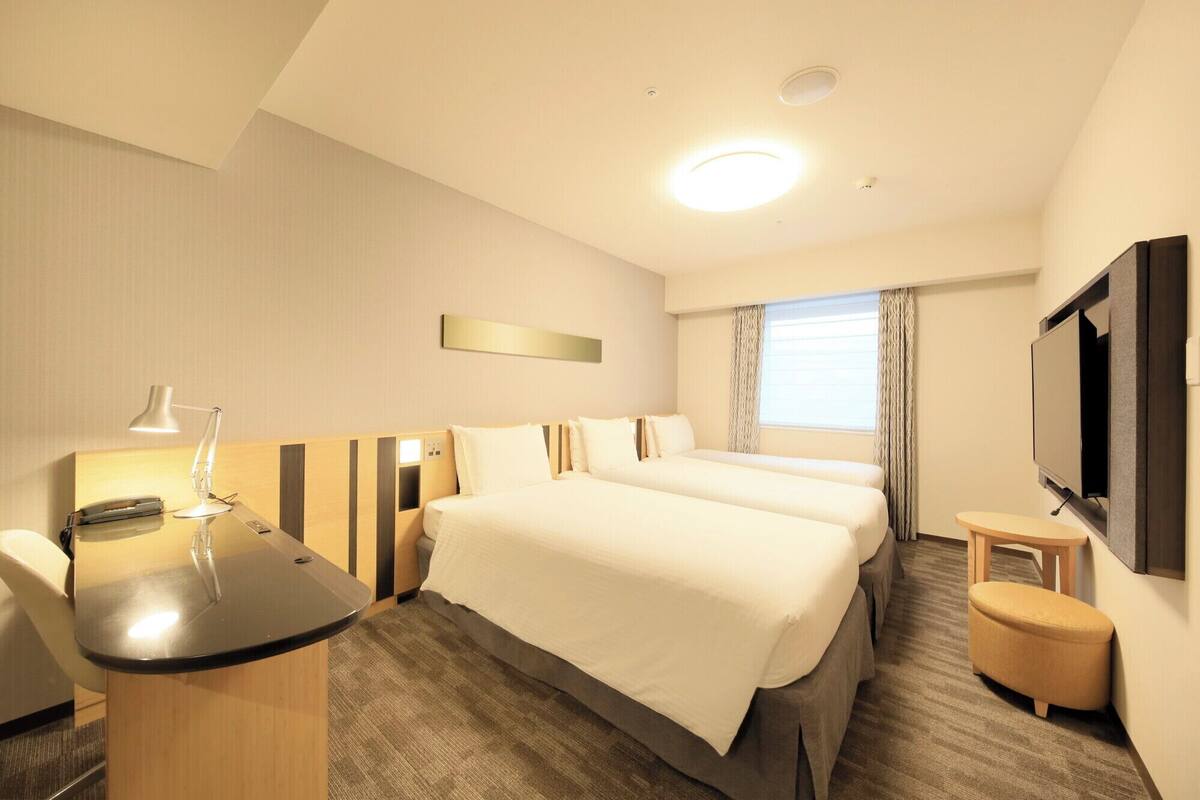 A hotel room with a bed, desk, chair, TV, and a small table.