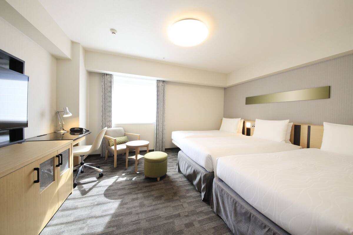 A hotel room with a bed, desk, chair, and TV.