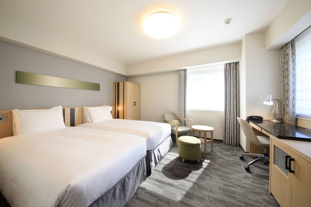 A hotel room with two beds, a desk, a chair, and a small table.