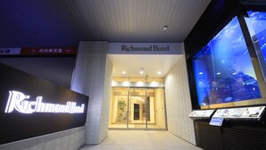 El exterior del Hotel Richmond con un gran letrero iluminado, un área de recepción con puertas de vidrio y una exhibición de acuario.
