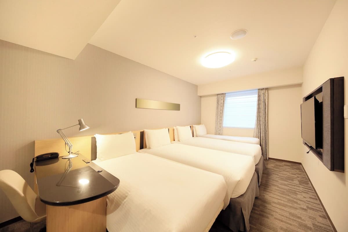 A hotel room with two beds, a desk with a lamp, a TV, and a window with curtains.