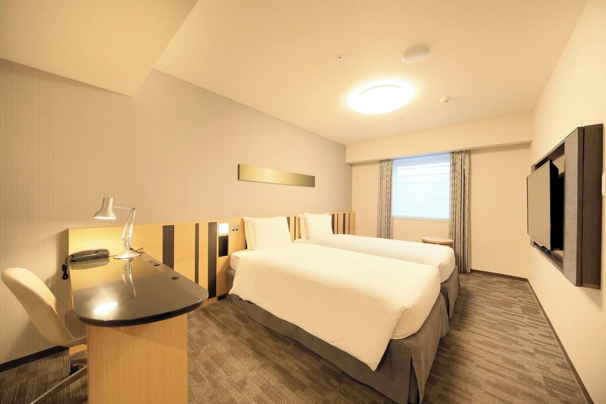 A hotel room with a bed, desk, chair, and a TV.