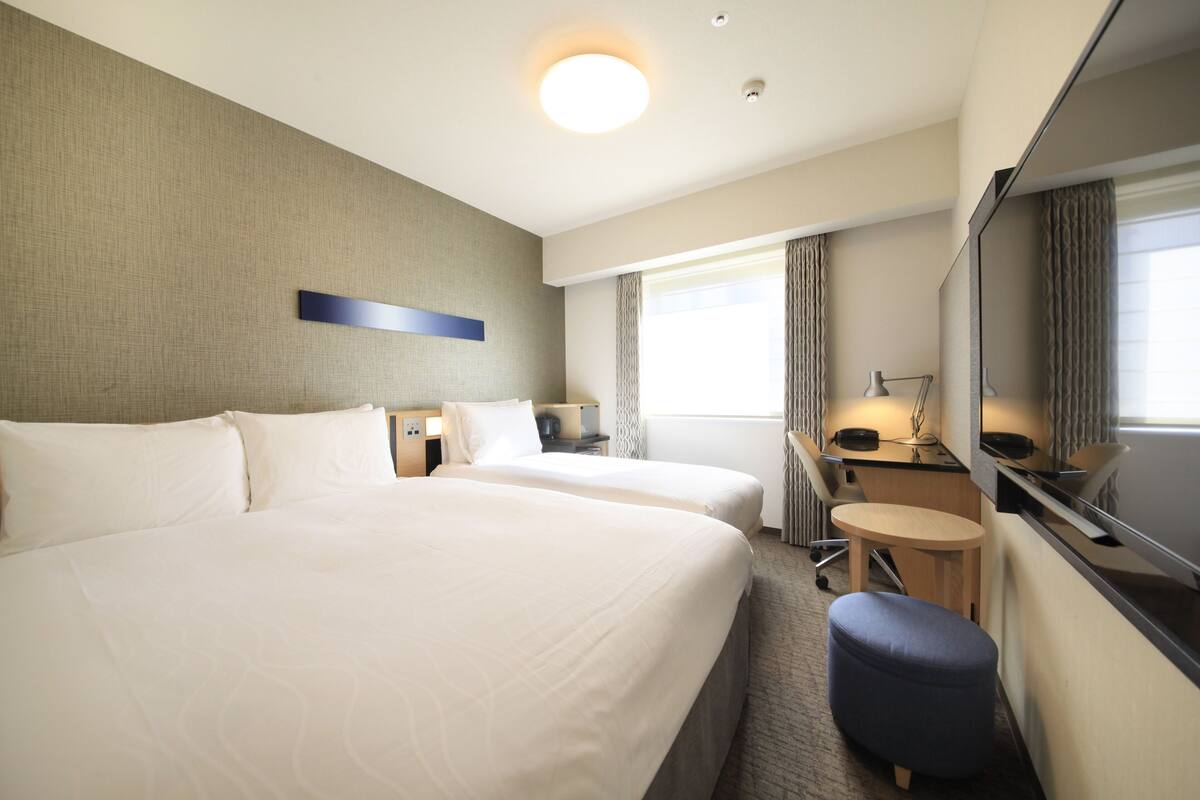 A hotel room with two beds, a desk, a chair, a mirror, and a window with curtains.