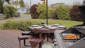 Een barbecue-opstelling met een grill, een tafel met borden en een wijnglas, en een rode parasol.