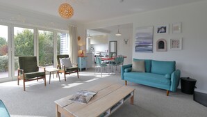 Een moderne woonkamer met een blauwgroene bank, een houten salontafel en een eethoek met stoelen.