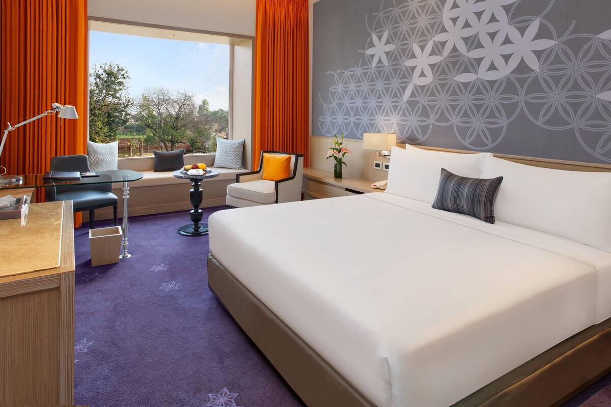 A hotel room with a large bed, a desk with a chair, a small table, and a window with curtains.