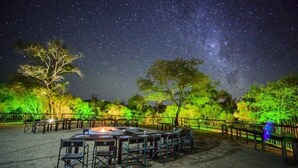 An outdoor dining area with tables and chairs, surrounded by a fence, under a starry night sky. - Shalati Kruger Lodge (Hluvukani)
