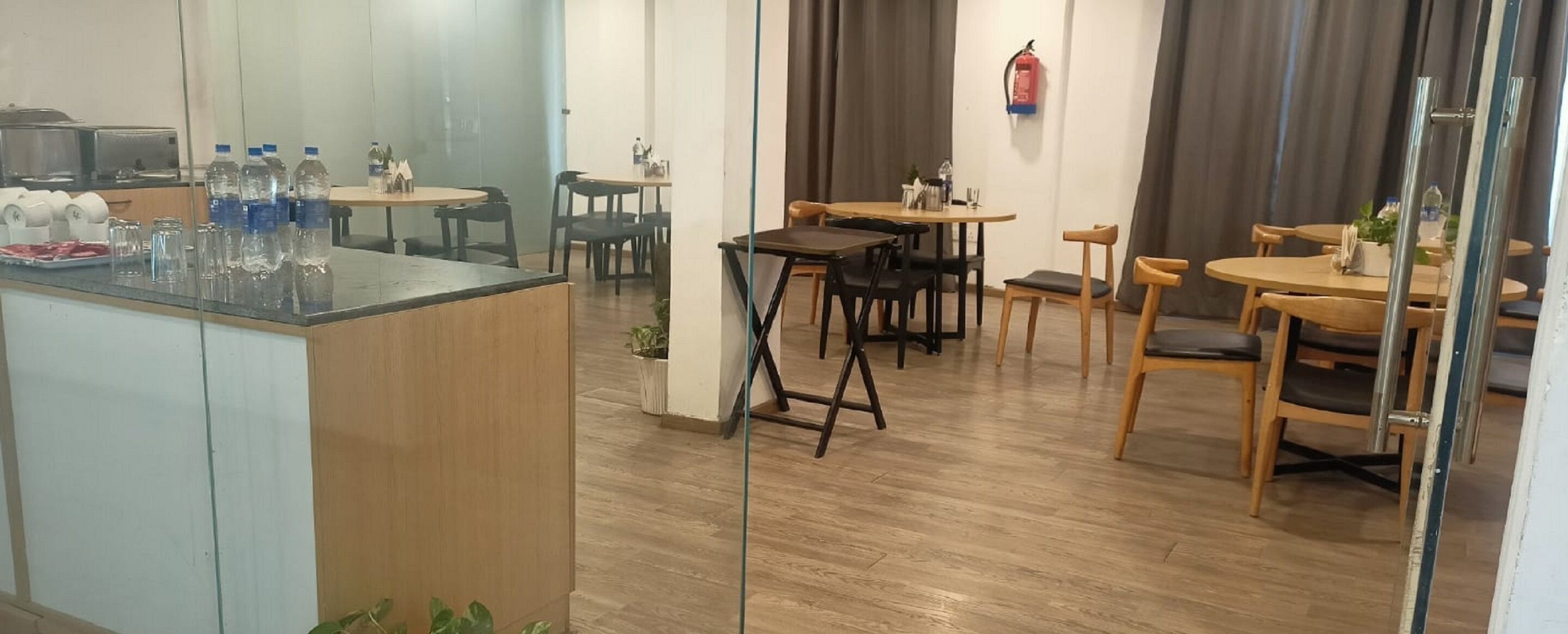 A hotel dining area with wooden tables and chairs, a central island with a bar, and a fire extinguisher on the wall.