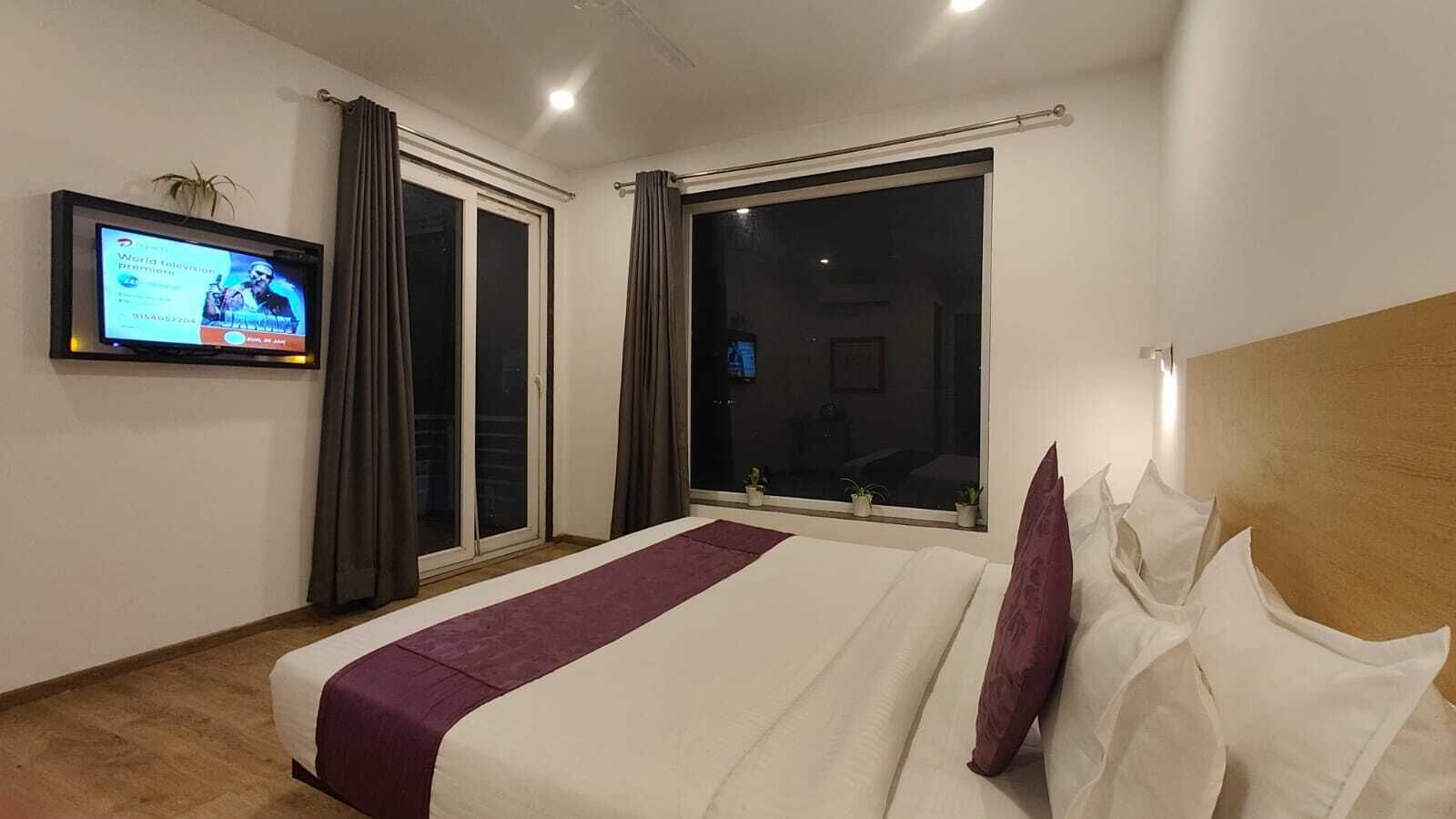 A hotel room with a large bed, a television on the wall, and a window with curtains.