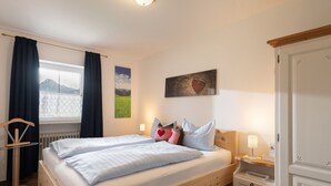 Cama doble con sábanas blancas, mesita de noche con lámpara, armario y ventana con cortinas.