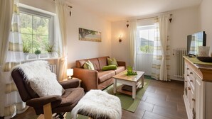 Una sala de estar acogedora con un sofá de cuero marrón, un sillón blanco y mullido, una mesita con un letrero que dice 'Relax' y un televisor sobre un mueble de madera.