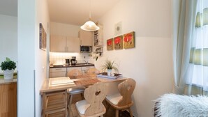 Cocina compacta con gabinetes de madera, microondas y cafetera. Hay tres sillas alrededor de una pequeña mesa de comedor, y una lámpara colgante arriba.