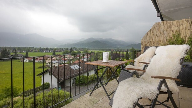 Un balcón con vistas a un pueblo y montañas, amueblado con una mesa y dos sillas.