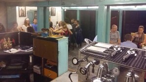 A room with a kitchenette, a dining table, and a group of people gathered around. - The Hotel Bandipur (Bandipur)