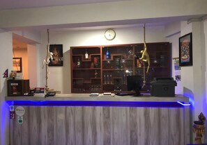 A bar area with a wooden counter, blue LED lighting, a clock, and various items on shelves. - The Hotel Bandipur (Bandipur)