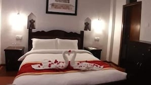 A hotel room with a bed, a ceiling fan, two bedside lamps, a framed picture on the wall, and a wooden wardrobe. - The Hotel Bandipur (Bandipur)