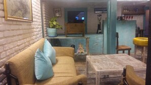 A cozy living room with a sofa, a small table, a potted plant, and a wooden chair. - The Hotel Bandipur (Bandipur)