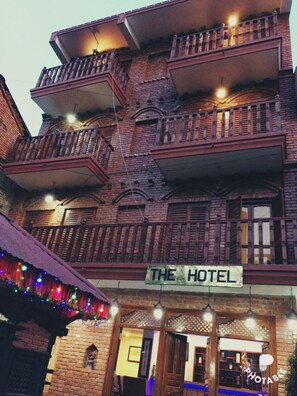 A multi-story building with a sign reading "THE HOTEL" at the ground level. The building features a brick facade with wooden balconies. - The Hotel Bandipur (Bandipur)