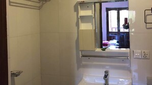 A bathroom with a white sink, a mirror, and a towel rack. - The Hotel Bandipur (Bandipur)