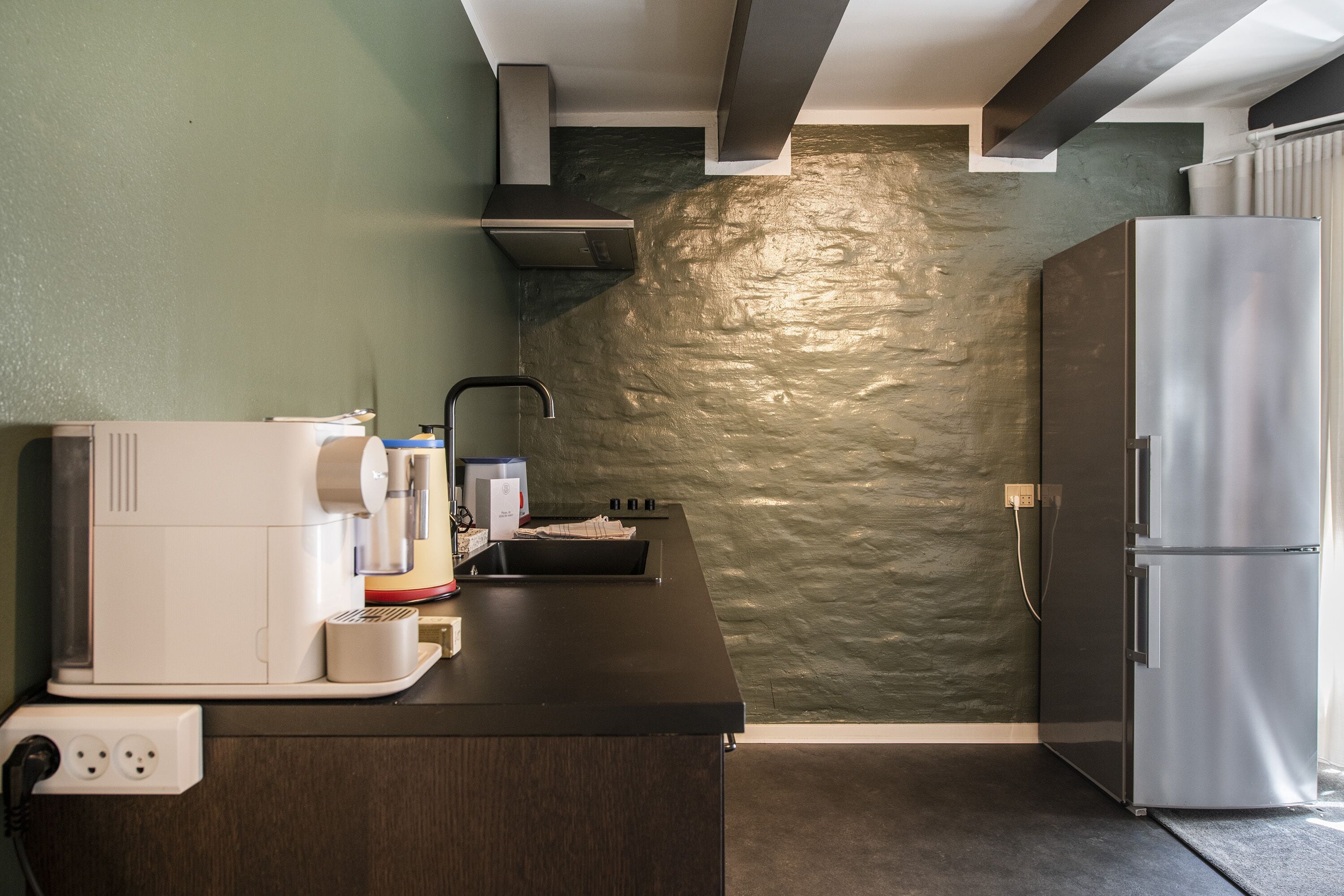 Una cocina con salpicadero de piedra, horno empotrado, refrigerador y cafetera en la encimera.