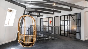 A spacious room with a high ceiling, exposed beams, a large window, and a hanging wicker chair. - The Churchill Penthouse by Daniel&Jacob’s (Copenhagen)