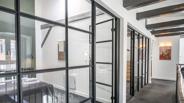 A modern hotel corridor with glass doors leading to a bedroom with a bed and a radiator. - The Churchill Penthouse by Daniel&Jacob’s (Copenhagen)