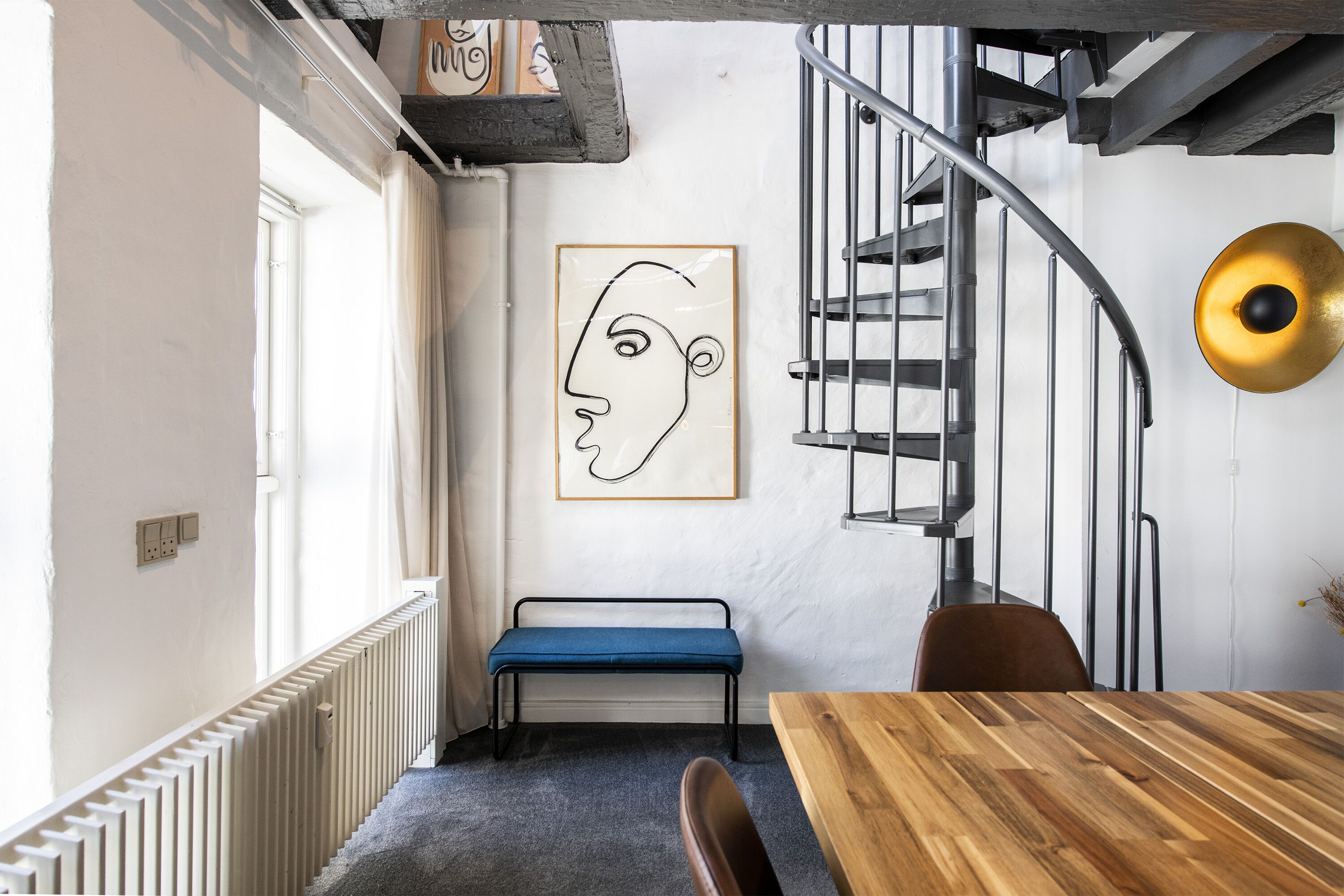 Un interior modern amb una escala espiraltraire, una banca blava i una taula de fusta.