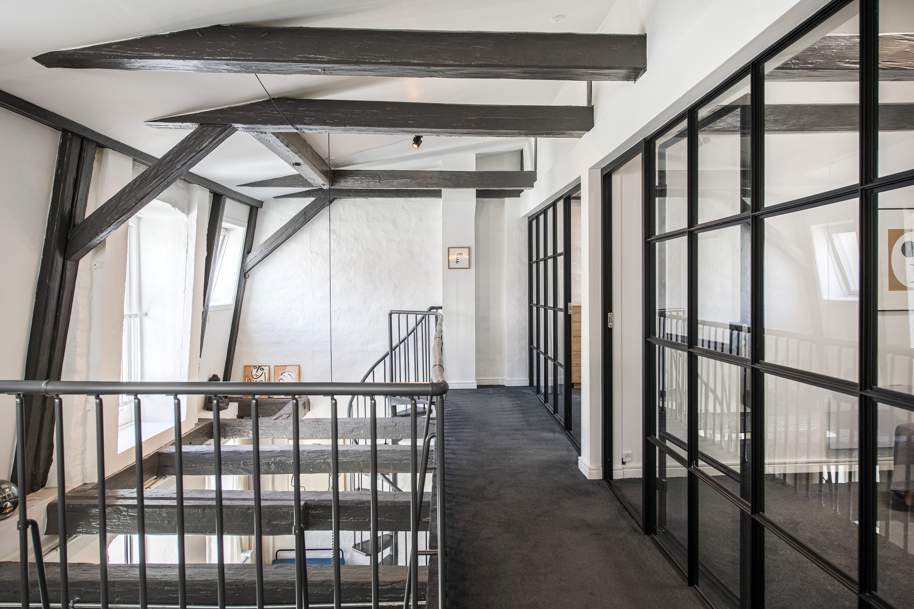 Un interior moderno con vigas a la vista, una escalera y ventanas amplias.