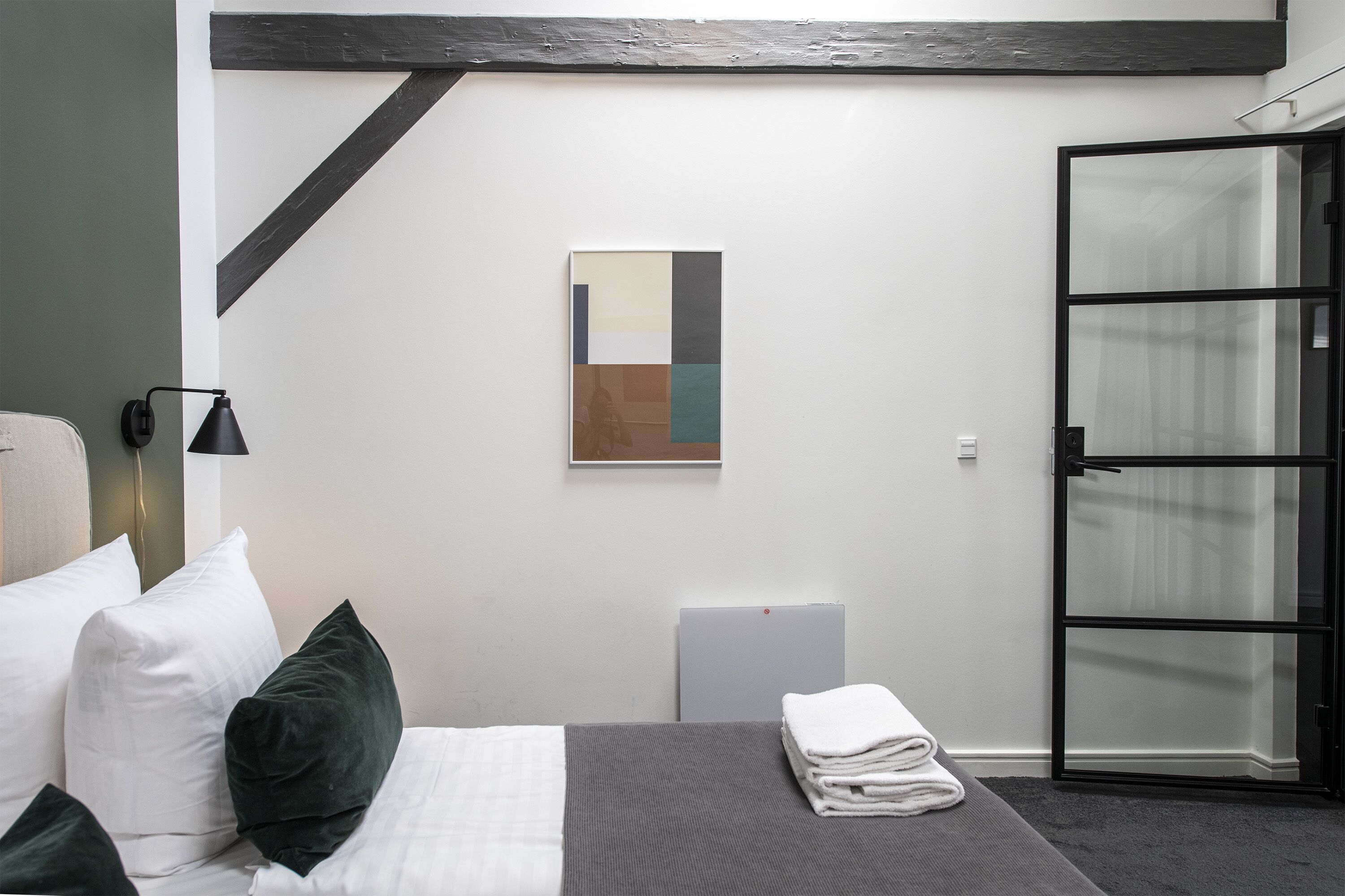 Una habitación de hotel moderna con cama, mesita de noche, una obra de arte en la pared y puerta corredera de vidrio.