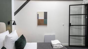 Una habitación de hotel moderna con cama, mesita de noche, una obra de arte en la pared y puerta corredera de vidrio.