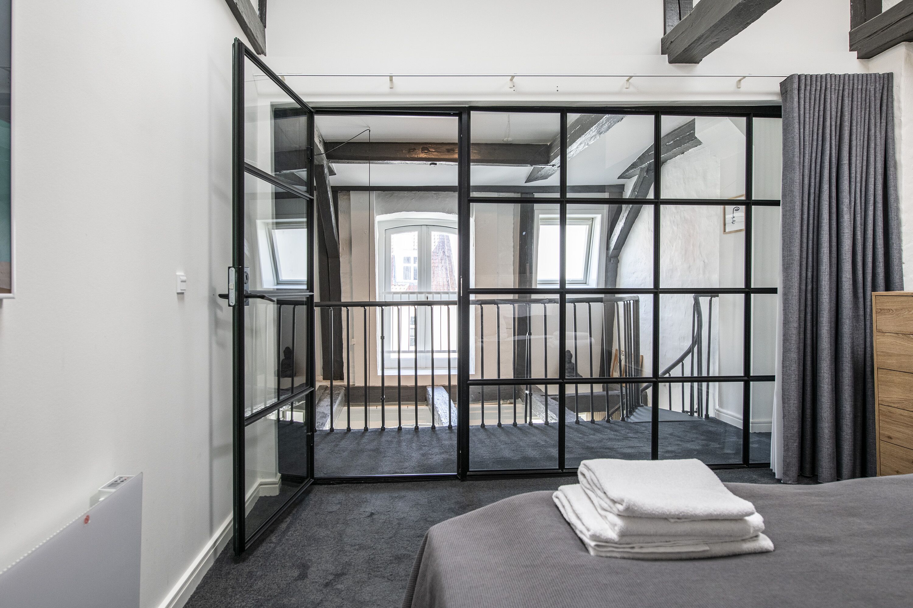 A modern hotel room with a balcony, a bed with neatly folded white towels, and a view of the cityscape through large windows.