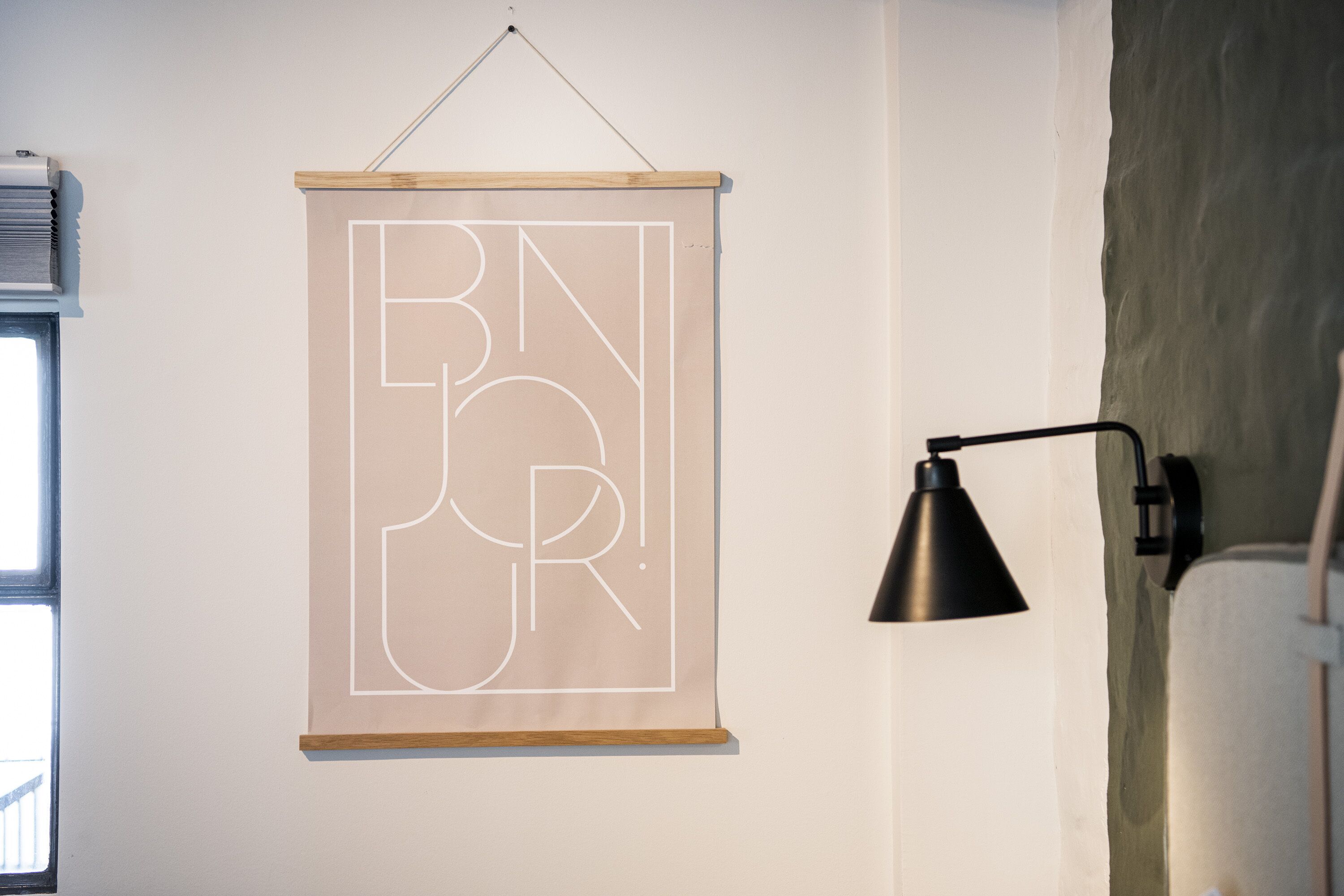 A minimalist room with a hanging abstract artwork, a black desk lamp, and a window with blinds.