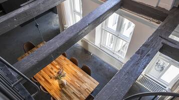 A wooden dining table with chairs, a hanging plant, and a view of a window and radiator.