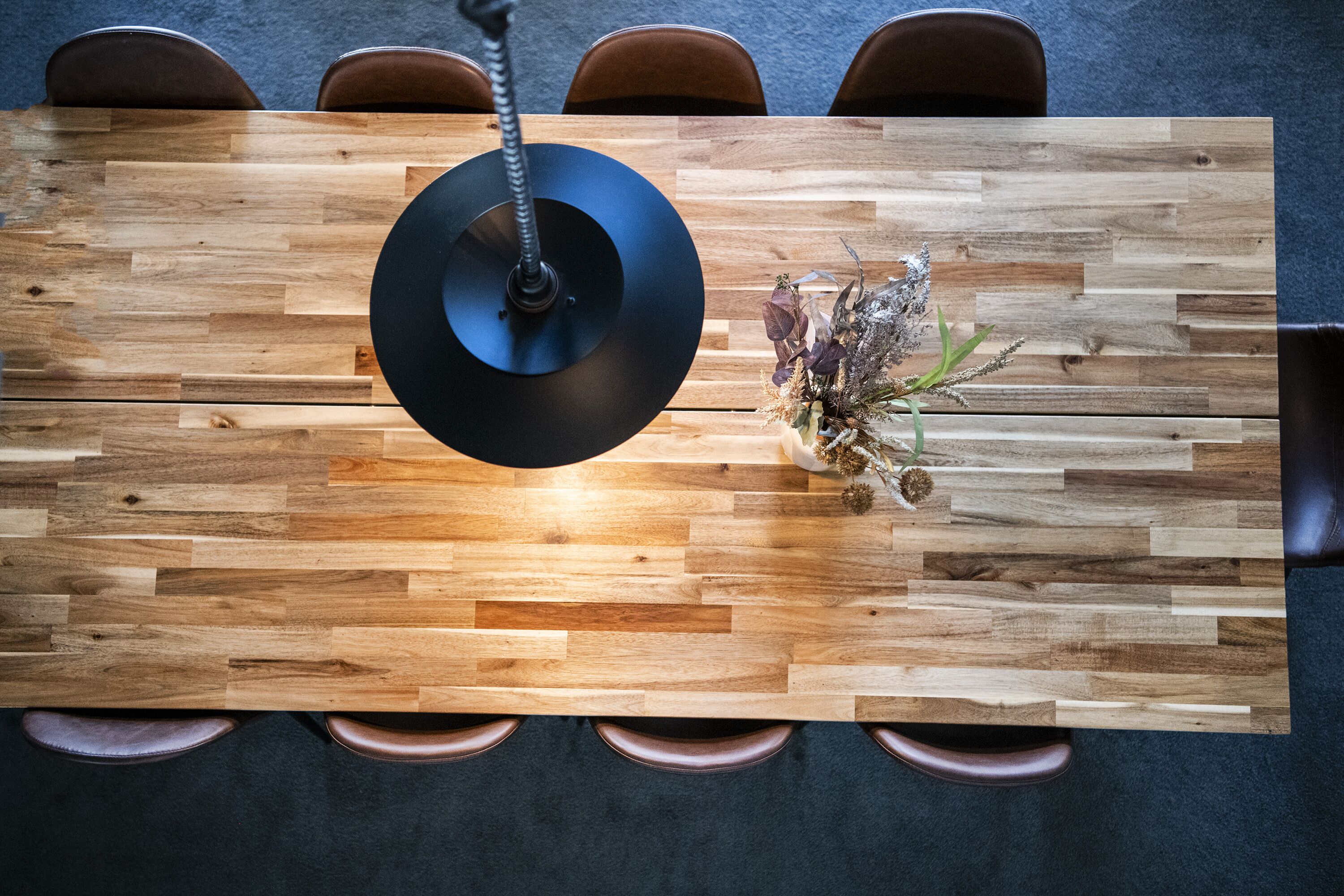 A wooden table with a black hanging lamp, surrounded by brown chairs.