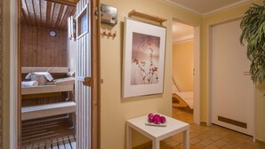 A wooden sauna with a clock, a framed picture on the wall, and a small table with pink ornaments. - Charming vacation apartment in Inntal ,with microwave,wifi,for2-4 guests,on 2 floors/15 (Oberaudorf)