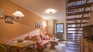 A cozy living room with a sofa, dining table, and chairs, a staircase, and a TV. - Charming vacation apartment in Inntal ,with microwave,wifi,for2-4 guests,on 2 floors/15 (Oberaudorf)