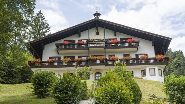 A two-story building with balconies adorned with flower boxes, a central entrance, and a surrounding garden. - Charming vacation apartment in Inntal ,with microwave,wifi,for2-4 guests,on 2 floors/15 (Oberaudorf)