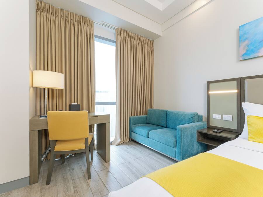 A hotel room with a bed, a desk with a chair, a sofa, a TV, and curtains.