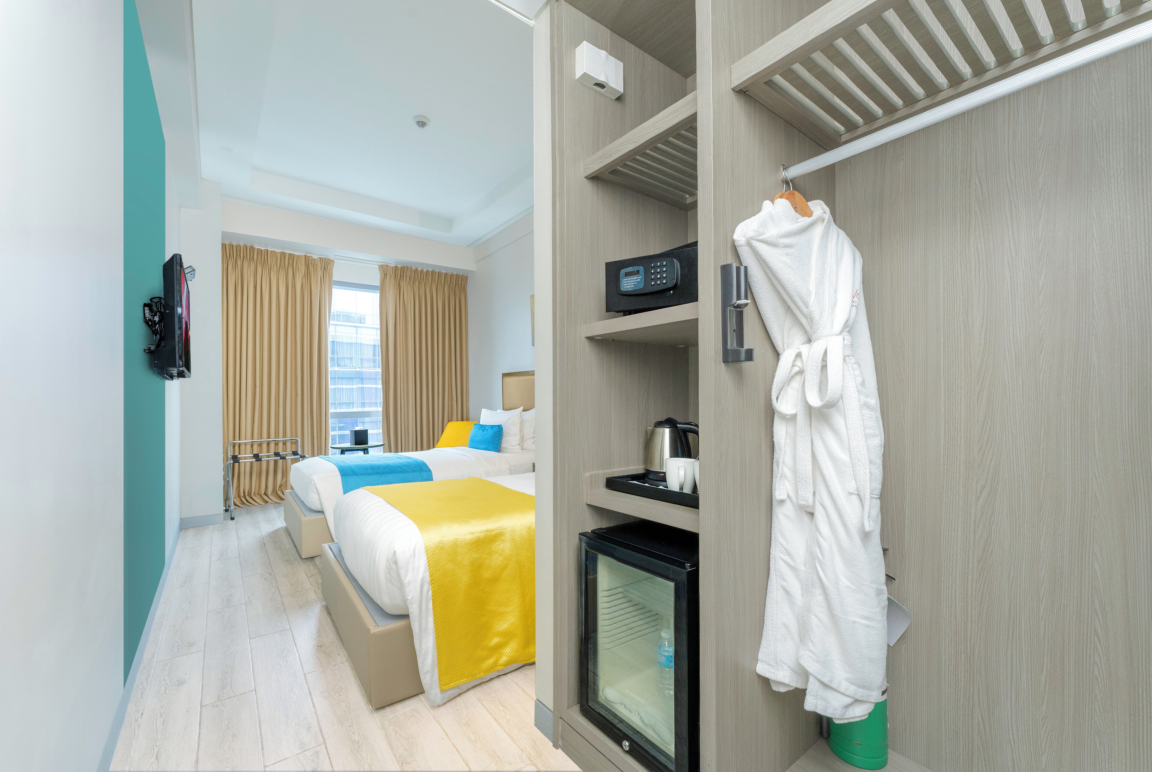 Habitación de hotel con cama, minibar, televisión y bata colgada en un perchero.