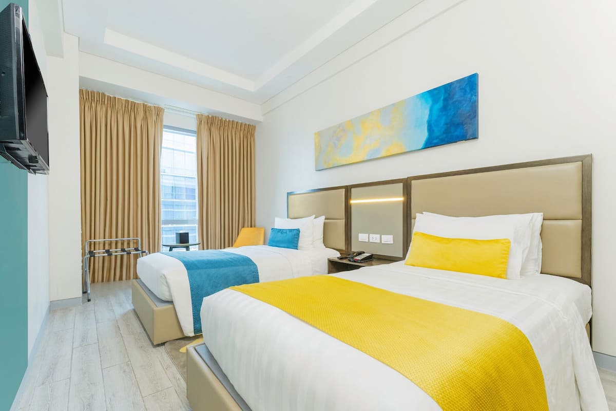 Une chambre d’hôtel avec deux lits, une télévision, un tableau et une fenêtre avec des rideaux.