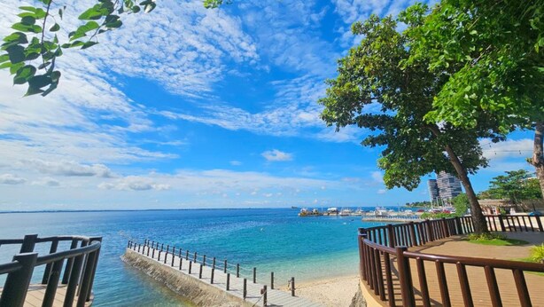 A coastal walkway with a wooden deck, a sandy beach, and a clear blue sky.